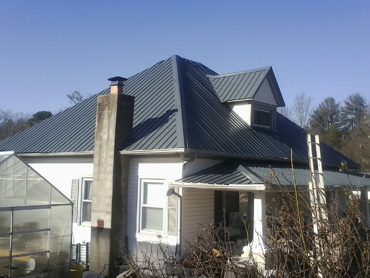 Dark blue standing seam metal roof on a white farmhouse with dormer — Slate & Tile Roof Repair by Roofing Brothers in Toston
