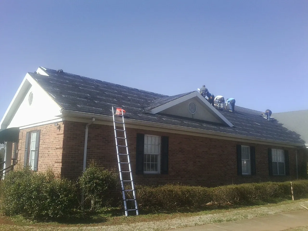 Crew tearing shingles off a brick ranch roof with a ladder set — Metal Roof Repair work by our crew in Toston