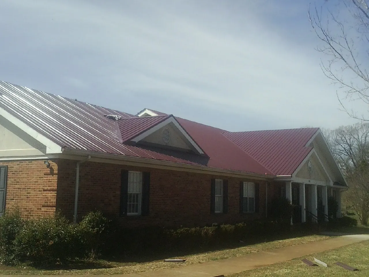 Red metal roof with gabled entries on a long brick building, from a Hail Damage Roof Repair job in Toston