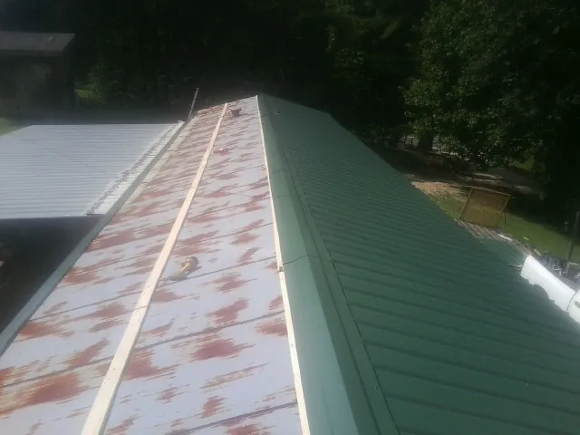 Old rusted panels beside newly installed green metal roofing — Wind Damage Roof Repair by Roofing Brothers in Toston
