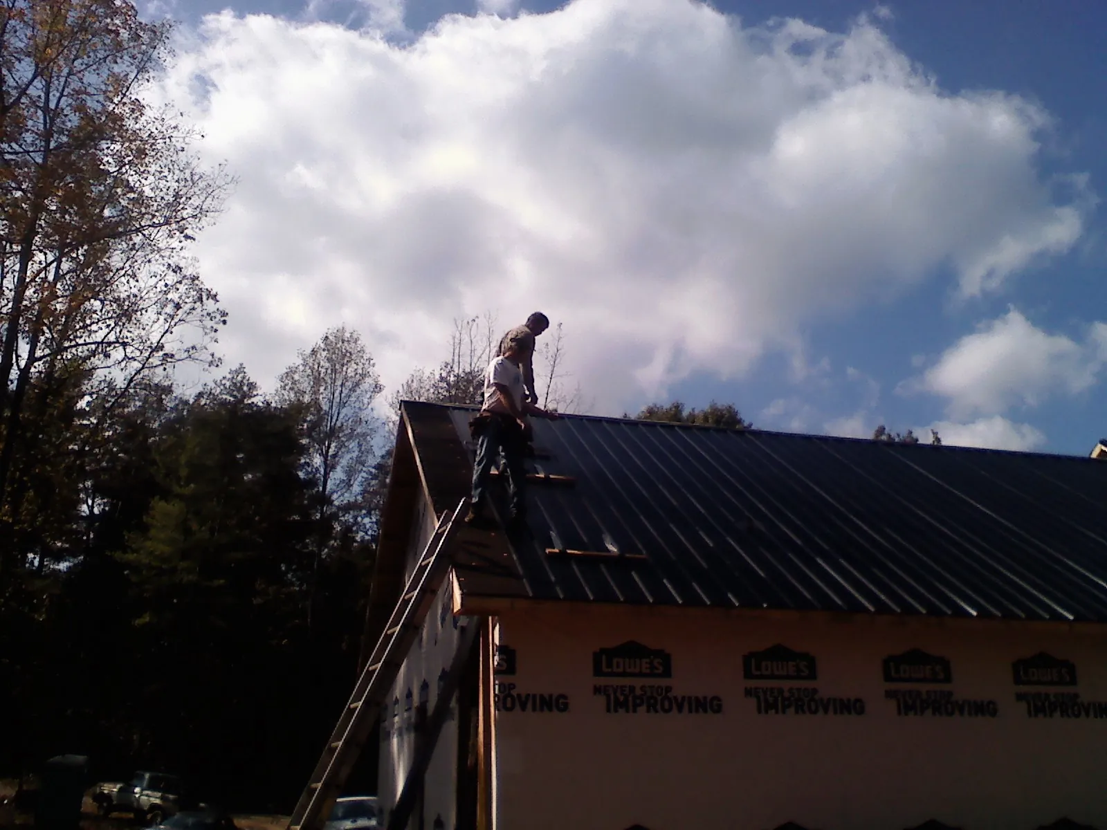 Roofer fastening dark metal panels high against a cloudy sky, from a Roof Inspection job in Toston