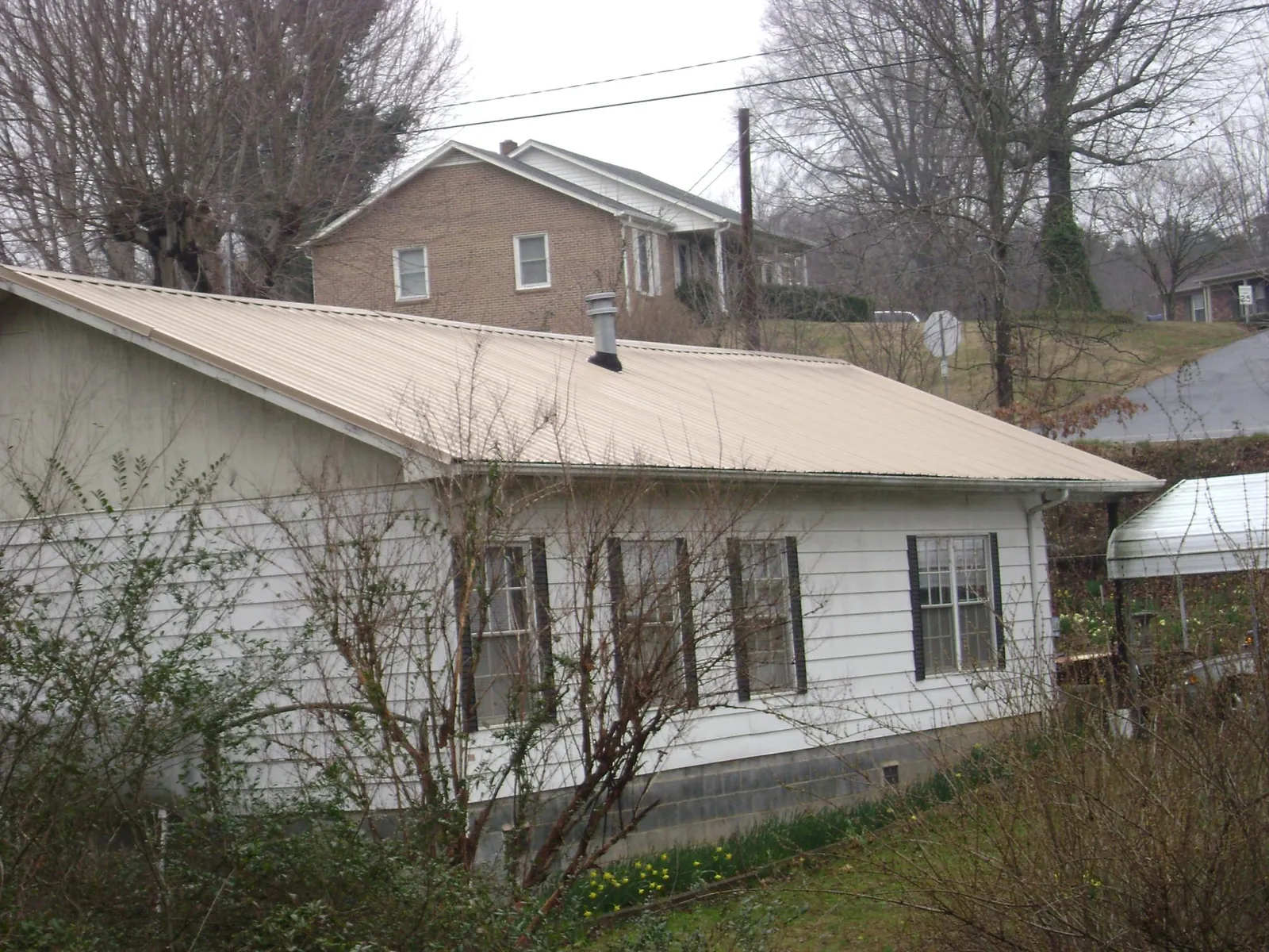 Tan metal roof on a white sided house set into a hillside — Commercial Roofing by Roofing Brothers in Toston