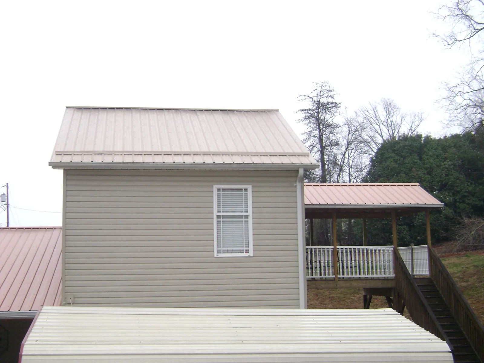 Tan metal roofs on a two story addition and attached porch, from a Roof Replacement job in Toston